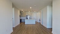 This well-appointed single-floor residence offers a clean, contemporary design with an open-concept layout that seamlessly connects the kitchen, dining, and living areas. Warm wood-look luxury vinyl plank flooring runs throughout the main living spaces, complemented by recessed lighting and crisp white walls that create a bright, airy atmosphere. The living area features a ceiling fan and a set of French doors that open to a private balcony, filling the space with natural light and providing outdoor access.

The kitchen is a standout feature, showcasing soft gray shaker-style cabinetry with matte black hardware, granite countertops, and a full white tile backsplash. A central island with an undermount sink and pendant lighting above serves as both a prep space and a gathering point. Stainless steel appliances, including a refrigerator with ice and water dispenser, a range, microwave, and dishwasher, complete the space. An in-unit washer is also conveniently located nearby.

The bathrooms are finished with granite-topped vanities, gray cabinetry, and wood-look flooring. The primary bath includes a glass-enclosed walk-in shower with tile surround and direct access to a spacious walk-in closet with built-in shelving and hanging rods. Secondary bedrooms feature plush carpeting, ceiling fans, and ample natural light from large windows.
