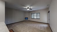 This single-floor residence offers a thoughtfully arranged layout with consistent finishes throughout. The main living area is generously proportioned, featuring soft wall-to-wall carpeting, a ceiling fan with integrated lighting, and a sleek corner-mounted electric fireplace that serves as a focal point. A window with horizontal blinds allows natural light to fill the space, creating a warm and comfortable ambiance.

The open-concept design flows seamlessly into a galley-style kitchen, which is equipped with dark cabinetry, black appliances including a side-by-side refrigerator with ice dispenser, and a smooth countertop surface. The kitchen is finished with durable hardwood-style flooring, offering a practical contrast to the carpeted living areas.

Additional rooms provide flexible living space, each featuring ceiling fans and windows with blinds that invite natural light. One room offers direct access to an exterior balcony through a glass-paneled door, extending the living experience outdoors.

The bathroom is finished with tile flooring, granite countertops, dark wood vanity cabinetry, and chrome hardware accents, delivering a clean and functional aesthetic. Throughout the residence, dark baseboards and door trim provide a cohesive design element that ties each room together, contributing to a polished and well-appointed interior.