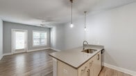 Located at 1871 Ashley River Rd in Charleston, SC, this single-floor, one-bedroom, one-bathroom residence offers a well-designed layout that maximizes comfort and functionality. The kitchen is a standout feature, showcasing light wood cabinetry, quartz countertops, a subway tile backsplash, and a full suite of stainless steel appliances including a refrigerator, range, and microwave. A peninsula with pendant lighting and a single-basin sink opens directly to the living area, creating a seamless flow ideal for everyday living. The living room benefits from natural light through a window fitted with blinds and is equipped with a ceiling fan. The bedroom is a comfortable retreat with plush carpeting, a ceiling fan, a large window overlooking greenery, and access to a spacious walk-in closet outfitted with wire shelving. The bathroom features wood-look tile flooring, a single-sink vanity with light cabinetry and quartz countertop, a large mirror, and a tub-shower combination. A dedicated laundry room houses a full-size washer and dryer. Wood-look flooring flows throughout the main living areas, and a neutral gray palette gives the entire space a clean, modern aesthetic.