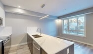Located in West Garneau, this thoughtfully designed 2-bedroom, 2-bathroom unit offers a modern aesthetic with high-quality finishes throughout. Light-toned luxury vinyl plank flooring flows seamlessly across the entire floor plan, complemented by neutral grey walls and clean white trim that create a bright, cohesive atmosphere.

The kitchen serves as a central highlight, featuring a large waterfall-edge quartz island with a double undermount sink, dark wood-grain lower cabinetry, white upper cabinetry, and a full suite of stainless steel appliances including a refrigerator, built-in microwave, dishwasher, and range. Pendant and recessed lighting illuminate the space with a contemporary touch.

A well-organized hallway connects the main living areas to the two bedrooms. The primary bedroom offers a comfortable footprint with a large window overlooking the neighbourhood streetscape, providing ample natural light. The second bedroom is similarly finished, offering a versatile and functional space.

Both bathrooms are finished to a modern standard, each featuring a soaker tub with a glass shower enclosure, white tile surround, large-format floor tiles, a wood-grain vanity with an integrated white sink, and a backlit mirror. The overall design of this unit prioritizes clean lines, functional efficiency, and a polished contemporary style.