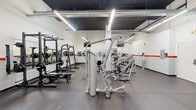 Located at 1000 Diamond St in Philadelphia's 19122 neighborhood, this fitness facility is a single-floor gym offering a spacious, open-plan layout designed to accommodate a full range of workout activities. The interior features clean white walls accented by a bold red stripe running along the perimeter, giving the space a modern, energetic aesthetic. The exposed ceiling is finished in dark paint, with visible ductwork and bright linear LED lighting that ensures the entire floor is evenly and amply illuminated.

The facility is well-stocked with a comprehensive selection of Hoist and TAG strength machines, including cable systems, leg press and curl machines, chest press stations, and multi-functional cable units. A dedicated free weights area houses a full dumbbell rack alongside benches, while a power rack with an Olympic barbell setup supports serious strength training. The cardio zone features Spirit treadmills and stationary cycling bikes, positioned alongside wall-length mirrors that enhance the sense of space and allow users to monitor their form. Durable rubber flooring covers the entire workout area, providing both safety and comfort. The facility includes a wall-mounted TV, a fire suppression system, wall-mounted sanitizer stations, and clearly posted rules, reflecting a commitment to a safe and orderly training environment.