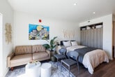 Located at 2121 Wood St in Oakland, CA, this efficiently designed studio offers a smart, modern layout that maximizes every square foot of its single-floor footprint. The open-plan living and sleeping area is anchored by warm wood-tone flooring, clean white walls, and a large window that floods the space with natural light while framing views of the surrounding Oakland cityscape.

The galley-style kitchen is thoughtfully outfitted with full-height upper cabinetry in a light wood finish, sleek gray lower cabinets, white quartz countertops, and a full suite of stainless steel appliances — including a range, over-range microwave, refrigerator, and dishwasher — providing a fully functional cooking space despite its compact form.

The sleeping area features a built-in wardrobe with integrated shelving above, offering practical storage solutions. Recessed lighting and high ceilings contribute to an airy, open ambiance throughout.

The bathroom is finished with light-toned tile flooring, a modern vanity with a white countertop, a large mirror with an adjacent medicine cabinet, and a shower/tub combination. The overall design aesthetic throughout the unit is contemporary and cohesive, with neutral tones and modern fixtures creating a clean, livable environment well-suited to urban living in Oakland.