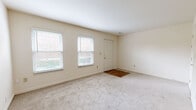 This two-story home offers a functional and well-proportioned layout spread across two floors. The main level, which makes up the larger portion of the home, features an entrance, a bright and open living room with plush carpeting and multiple windows that invite natural light, a kitchen, and a bathroom. The kitchen is equipped with light wood cabinetry, granite-style countertops, a peninsula breakfast bar, wood-look flooring, and black appliances including a refrigerator, range, microwave, and dishwasher. The living room is generously sized with neutral carpet and clean white walls, creating a versatile and welcoming space. A staircase leads to the upper level, which houses both bedrooms, a second bathroom, hallways, and a utility room. The primary bedroom is a comfortable size and features carpeting, multiple windows with natural light, and access to a well-organized walk-in closet with built-in shelving, hanging rods, and drawers. The second bedroom also features carpet and windows. Both bathrooms include wood-toned vanities with white countertops and mirrors. The home's neutral color palette and consistent finishes throughout give it a clean, cohesive feel.