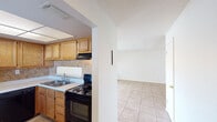 The Summit West Apartments Two Bedroom B1 floor plan offers a well-organized, single-story layout designed for comfortable everyday living. The kitchen is equipped with warm oak cabinetry, a tile backsplash, white countertops, a double-basin sink, and black appliances including a refrigerator, electric range, and dishwasher. Tile flooring runs throughout the kitchen, providing a practical and easy-to-maintain surface. The living area is bright and open, featuring tile flooring, a ceiling fan with light fixture, and a sliding glass door fitted with vertical blinds that leads directly to a private enclosed patio. The patio is bordered by a painted cinder block wall, offering a sense of privacy while allowing views of mature surrounding trees. Both bedrooms feature rich dark wood-style laminate flooring, ceiling fans, and windows with blinds that allow for natural light and ventilation. A shared full bathroom includes a single-sink vanity with oak cabinetry, a large mirror with overhead lighting, and a shower-tub combination. The textured ceilings are consistent throughout the unit, contributing to a cohesive aesthetic. This two-bedroom layout provides a practical and comfortable living environment within the Summit West Apartments community.