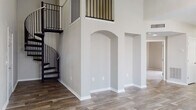 Located in Tampa, Florida, this two-story residence offers a thoughtfully designed layout that balances open living areas with functional, well-appointed spaces. The main living area immediately impresses with soaring double-height ceilings, elegant arched wall niches, and rich wood-look flooring that flows throughout the main level. A striking wrought-iron spiral staircase serves as a dramatic architectural centerpiece, connecting the two floors with both style and practicality.

The kitchen is outfitted with crisp white shaker cabinetry, light stone countertops, a classic subway tile backsplash, and stainless steel appliances, including a range, over-the-range microwave, and dishwasher. A pass-through window with pendant lighting connects the kitchen to the living and dining areas, enhancing the open, airy feel.

The upper level features generously sized bedrooms with vaulted ceilings, ceiling fans, and an abundance of natural light streaming through large windows. One bedroom showcases plush carpeting, while others continue the wood-look flooring found below. The full bathroom includes a dual-sink vanity with white cabinetry, stone countertops, a soaking tub and shower combination, and coordinating wood-look tile flooring. A dedicated laundry area with shelving and washer/dryer hookups adds everyday convenience to this well-rounded home.