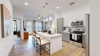 Located at 5750 Airport Rd in Santa Fe, NM, this thoughtfully designed one-bedroom, one-bathroom residence offers a cohesive, modern aesthetic across its efficiently laid-out single floor. The open-concept kitchen and living area serves as the heart of the home, anchored by a central island with seating — ideal for casual dining or entertaining. The kitchen is outfitted with stainless steel appliances, including a side-by-side refrigerator, range, and over-the-range microwave, complemented by two-tone gray and white cabinetry, marble-style tile backsplash, and crisp white countertops. Light wood-style flooring runs throughout the main living areas, enhancing the bright, airy atmosphere. A built-in entry nook with shelving and a bench provides a practical drop zone. The living room is generously sized with large windows and a glass-panel door that invite natural light and outdoor views. The bedroom features plush carpet, a ceiling fan, and a window with outdoor views, offering a calm retreat. A dedicated closet provides ample storage. The bathroom is finished with a glass-enclosed walk-in shower, gray vanity cabinetry with white countertop, and wood-look flooring, creating a clean, spa-like feel throughout.