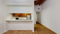 This two-floor residence showcases a distinctive architectural character defined by dramatic exposed wood beam ceilings that lend warmth and a loft-like ambiance to the main living areas. The entryway makes a strong first impression with a stately wood panel door flanked by floor-to-ceiling sidelights, terracotta tile flooring, and an industrial-style pendant light overhead, offering a welcoming transition into the home.

The open living areas feature hardwood-style flooring throughout, with clean white walls that enhance the sense of openness and height. A pass-through kitchen connects seamlessly to the living space, equipped with warm honey-toned wood cabinetry, white stone countertops, stainless steel appliances including a refrigerator and range with overhead ventilation, providing a functional and well-appointed cooking environment.

Carpeted areas on the upper level offer comfortable, quieter spaces suited for bedrooms, while additional rooms on both floors feature the same rich hardwood-style flooring. Large multi-pane windows bring in natural light and offer views to the exterior.

The bathrooms are finished with tile flooring, wood vanities topped with stone countertops, and clean white fixtures. One bathroom features a full tub and shower combination with classic white tile surround, while another presents a half-bath layout. The dollhouse view confirms a well-organized, multi-room floor plan across two levels.