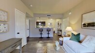 This single-story residence offers three bedrooms and two bathrooms within a thoughtfully designed floor plan. The open-concept living and dining area serves as the heart of the home, featuring wood-style flooring, neutral-toned walls, and a ceiling fan overhead. Large windows along the front wall allow natural light to fill the space, creating a bright and welcoming atmosphere.

The kitchen is positioned adjacent to the living area and is outfitted with dark espresso cabinetry, granite-style countertops, stainless steel appliances including a microwave and dishwasher, and a raised breakfast bar with bar seating. Light wood-style flooring continues throughout the kitchen, which also accommodates a small dining nook near the entry.

The primary bedroom is a well-sized retreat featuring plush carpeting, a ceiling fan, and multiple windows that invite natural light. The additional bedrooms are similarly carpeted and comfortably scaled. A dedicated walk-in closet provides generous storage with a full-length hanging rod and upper shelving. Both bathrooms feature dark cabinetry paired with granite countertops, wood-style flooring, and a tub-shower combination. An in-unit laundry area completes this efficiently arranged home.