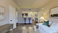 This single-story residence offers three bedrooms and two bathrooms within a thoughtfully designed floor plan. The open-concept living and dining area serves as the heart of the home, featuring wood-style flooring, neutral-toned walls, and a ceiling fan overhead. Large windows along the front wall allow natural light to fill the space, creating a bright and welcoming atmosphere.

The kitchen is positioned adjacent to the living area and is outfitted with dark espresso cabinetry, granite-style countertops, stainless steel appliances including a microwave and dishwasher, and a raised breakfast bar with bar seating. Light wood-style flooring continues throughout the kitchen, which also accommodates a small dining nook near the entry.

The primary bedroom is a well-sized retreat featuring plush carpeting, a ceiling fan, and multiple windows that invite natural light. The additional bedrooms are similarly carpeted and comfortably scaled. A dedicated walk-in closet provides generous storage with a full-length hanging rod and upper shelving. Both bathrooms feature dark cabinetry paired with granite countertops, wood-style flooring, and a tub-shower combination. An in-unit laundry area completes this efficiently arranged home.
