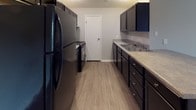 Located at 507 S Main St in Englewood, Ohio, this single-floor unit offers a well-organized layout designed for comfortable everyday living. The galley-style kitchen is a functional highlight, featuring dark cabinetry, light countertops, wood-look vinyl flooring, and black appliances including a refrigerator and range. A breakfast bar connects the kitchen to the open living area, which is carpeted and bathed in a neutral gray palette, creating a clean and welcoming atmosphere. Multiple bedrooms are finished with plush carpeting and neutral-toned walls, with several rooms featuring windows that invite natural light. Closet space is well-represented throughout, including a walk-in closet with wood-accented walls and built-in shelving in one of the bedrooms. The unit includes two bathrooms: one full bath with a tub-shower combo and wood-look flooring, and a second bathroom featuring bold tile-look wall accents, a white vanity with storage, and a large mirror. Consistent use of light gray walls, white trim, and wood-look vinyl flooring in wet areas gives the unit a cohesive, modern aesthetic throughout. The thoughtful layout and well-appointed finishes make this a practical and attractive space.