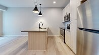 This single-floor space offers a thoughtfully designed interior defined by a clean, modern aesthetic and a cohesive neutral palette. Light wood laminate flooring runs throughout, lending warmth and continuity across all rooms.

The kitchen serves as a standout feature of the unit, outfitted with light wood cabinetry, a subway tile backsplash, and a full suite of stainless steel appliances including a refrigerator, electric range, and built-in microwave. A central island provides additional counter space and houses a black matte sink, complemented by a pair of stylish black pendant lights overhead. Ample upper and lower cabinetry offers generous storage, while the open layout connects the kitchen seamlessly to the adjacent living area.

The remaining rooms present versatile, unfurnished spaces with smooth, light grey walls, clean white baseboards, and the same warm wood flooring. Each room is equipped with standard electrical outlets, reflecting a functional and move-in-ready condition.

The 3D model reveals a compact but efficiently arranged floor plan, with a bathroom and additional enclosed rooms accessible off the main living space. The overall ambiance is bright, minimalist, and contemporary, making it well-suited for a variety of uses and personal styles.
