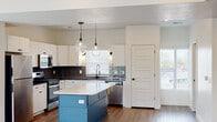 Located at 880 S State St in Clearfield, Utah, this contemporary multi-floor home spans three levels and showcases modern design details throughout. The heart of the home is a well-appointed kitchen featuring crisp white cabinetry, dark granite countertops, and a striking teal center island topped with a bright white surface. Stainless steel appliances, including a gas range, microwave, refrigerator, and dishwasher, complement the space, while decorative pendant lighting and mixed tile backsplashes add visual interest. Light wood-style flooring flows through the main living areas, which are filled with natural light from multiple windows and a sliding glass door that opens to a balcony with modern cable railing. A staircase with wood handrail and black metal balusters connects the floors. A convenient half bath on the main level features a pedestal sink with matte black fixtures. Upper-level bedrooms are carpeted and include a spacious walk-in closet with built-in shelving and a bench. A full bathroom showcases floor-to-ceiling white subway tile surrounding a soaking tub, complemented by matte black fixtures. Throughout the home, neutral tones, recessed lighting, and clean architectural lines create a cohesive, move-in-ready aesthetic.