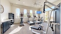 Located at 6201 W Oaks Blvd in Rocklin, CA, this fitness center offers a well-appointed exercise space designed to support a comprehensive workout experience. The single-floor layout is bright and open, featuring neutral-toned walls, textured carpet flooring, and recessed lighting complemented by a large ceiling fan that keeps the space comfortable during workouts.

Tall, arched windows along one wall flood the room with abundant natural light and provide views of the surrounding outdoor landscape, including palm trees and the adjacent outdoor area. A wall-mounted flat-screen television adds an entertainment option for cardio sessions.

The facility is outfitted with a well-rounded selection of exercise equipment, including multiple Star Trac treadmills, an elliptical cross-trainer, a stationary recumbent bike, a functional cable/multi-station strength machine, and various benches and resistance equipment. A large wall mirror in the strength training area enhances the sense of space and allows for form monitoring.

Along one wall, built-in navy cabinetry with a countertop provides storage, and a small beverage refrigerator is also present. Framed dog-themed artwork adds a playful, welcoming character to the space. Glass-paneled entry doors open to the exterior, further connecting the room to the outdoors. An all-gender restroom is conveniently accessible directly from the fitness area.