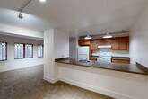 Located at 9615 Dewitt Dr in Silver Spring, MD, this one-bedroom, one-bathroom residence offers a thoughtfully arranged single-floor layout with a variety of architectural details that set it apart. The open-concept living, dining, and kitchen area forms the heart of the home, anchored by a peninsula breakfast bar with dark laminate countertops that separates the kitchen from the living space. The kitchen is well-appointed with warm honey-toned wood cabinetry, a full suite of white appliances including a refrigerator and electric range, and pendant lighting that adds a clean, finished look overhead. The living room is defined by a gracefully curved wall lined with distinctive Gothic-arched windows, allowing natural light to filter in and lending the space an elegant, character-rich quality. The bedroom is a comfortable size and features angled architectural ceiling details along with a window that brings in additional natural light. Three closets throughout the residence provide generous storage. Soft wall-to-wall carpeting runs through the living and sleeping areas, contributing to a warm and quiet ambiance. The entrance provides a welcoming transition into the home, with clean white walls and bright finishes carried consistently throughout the unit.