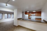 Located at 9615 Dewitt Dr in Silver Spring, MD, this one-bedroom, one-bathroom residence offers a thoughtfully arranged single-floor layout with a variety of architectural details that set it apart. The open-concept living, dining, and kitchen area forms the heart of the home, anchored by a peninsula breakfast bar with dark laminate countertops that separates the kitchen from the living space. The kitchen is well-appointed with warm honey-toned wood cabinetry, a full suite of white appliances including a refrigerator and electric range, and pendant lighting that adds a clean, finished look overhead. The living room is defined by a gracefully curved wall lined with distinctive Gothic-arched windows, allowing natural light to filter in and lending the space an elegant, character-rich quality. The bedroom is a comfortable size and features angled architectural ceiling details along with a window that brings in additional natural light. Three closets throughout the residence provide generous storage. Soft wall-to-wall carpeting runs through the living and sleeping areas, contributing to a warm and quiet ambiance. The entrance provides a welcoming transition into the home, with clean white walls and bright finishes carried consistently throughout the unit.
