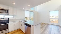 Located at 310 K St in Chula Vista, CA, this modern single-floor unit showcases a bright, open-concept layout with clean lines and contemporary finishes throughout. The living area stands out with dramatically tall ceilings and floor-to-ceiling windows that flood the space with natural light, while sliding glass doors open to a private balcony offering open views of the surrounding neighborhood. Light-toned hardwood-style flooring runs consistently throughout, creating a cohesive and airy feel. The kitchen is well-appointed with crisp white shaker cabinetry, neutral quartz-style countertops, a peninsula with a built-in sink and dishwasher, and a full suite of stainless steel appliances including a gas range, microwave, and refrigerator. Recessed lighting and a window above the range ensure the kitchen remains bright and functional. The bedrooms are generously sized, each featuring natural light from windows with outdoor views. One bedroom includes a built-in closet with shelving, offering practical storage solutions. The bathroom is finished with white cabinetry, a single undermount sink, neutral countertops, and large mirrors that enhance the sense of space. The unit's overall design emphasizes simplicity, brightness, and modern comfort throughout.