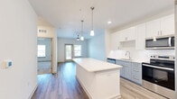 Located at 50 Lago Mar Way in Jacksonville, FL, this thoughtfully designed one-bedroom, one-bathroom residence offers a smart and efficient single-level floor plan. The open-concept living area seamlessly connects the kitchen, dining, and living spaces, creating a bright and airy atmosphere enhanced by light-toned walls and wood-style flooring throughout.

The kitchen is a standout feature, showcasing crisp white upper cabinetry, soft gray lower cabinets, a white quartz countertop island with pendant lighting above, and a full suite of stainless steel appliances including a refrigerator with ice maker, electric range, and built-in microwave. Recessed lighting and a clean white subway tile backsplash complete the modern aesthetic. The living area extends toward a glass door that invites natural light and outdoor access.

The bedroom is carpeted for comfort, features a ceiling fan, and includes a closet for storage. The bathroom is finished with light wood-look flooring, a quartz-topped white vanity, a tub/shower combination, and grab bars for added accessibility.

A dedicated in-unit laundry room with a full-size washer and dryer adds everyday convenience. The overall design is clean, contemporary, and move-in ready.