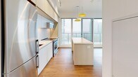 This thoughtfully designed 3-bedroom, 2-bathroom unit on a single floor offers a functional and modern living experience. The open-concept kitchen is a standout feature, finished with sleek white cabinetry extending to the ceiling, a marble-style backsplash, stainless steel appliances including a built-in oven and microwave, and a light wood center island with pendant lighting overhead. Floor-to-ceiling windows and sliding glass doors flood the kitchen and living area with natural light while providing access to a glass-railed balcony with sweeping urban views.

The three bedrooms are finished with warm hardwood-style flooring and crisp white walls. The primary bedroom features double doors and large windows overlooking the cityscape. The additional bedrooms are compact yet bright, each with windows that bring in natural light.

Both bathrooms are finished with large-format grey tile and feature clean, contemporary fixtures. One bathroom includes a deep soaking tub, while the other offers a walk-in shower with a lit vanity mirror and undermount sink. A stacked washer and dryer unit is conveniently tucked into a dedicated closet between the bathroom and living area, maximizing the efficient use of space throughout this well-appointed urban residence.
