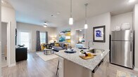 Located at 2619 Cottonwood Way in San Antonio, TX, this single-story, 2-bedroom, 2-bathroom residence offers a thoughtfully designed open-concept layout that seamlessly connects the kitchen, dining, and living areas. The kitchen is a standout feature, boasting granite countertops, gray shaker-style cabinetry, a decorative tile backsplash, stainless steel appliances, and a peninsula island with pendant lighting and bar seating — ideal for casual dining and entertaining. The adjoining living room is bright and inviting, with wood-style flooring and natural light filtering through large windows dressed with patterned curtains. Both bedrooms feature plush carpeting, ceiling fans, and generous natural light. The spacious primary bedroom includes a walk-in closet outfitted with wire shelving. Each bathroom mirrors the kitchen's refined aesthetic, with granite-topped vanities, gray cabinetry, and wood-style flooring. One bathroom features a tub-shower combination, while the other offers a shower with additional overhead storage. A dedicated walk-in closet with carpet flooring and wire shelving provides ample storage. Neutral wall tones and consistent modern finishes create a cohesive, contemporary ambiance throughout the entire space.