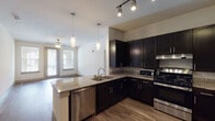 Located at 2255 Arkansas Ln in Grand Prairie, TX, this single-floor residence offers a well-designed layout with modern finishes throughout. The kitchen serves as a central highlight, featuring dark espresso cabinetry, granite countertops, a peninsula with an integrated sink and pendant lighting, and a full suite of stainless steel appliances including a gas range, microwave, dishwasher, and refrigerator. Track lighting above the kitchen adds functional illumination, while hardwood-style flooring extends through the main living areas, creating a cohesive and polished look. The living room is bright and open, with a ceiling fan, large windows with blinds that invite natural light, and an arched architectural detail that connects to the hallway. A corridor lined with doors leads to the private areas of the home, including a carpeted bedroom with a window offering outdoor views. The bathroom includes a glass-enclosed tiled shower, dark vanity cabinetry with granite counters, and direct access to a walk-in closet equipped with multi-level shelving rods and built-in storage. A secondary bathroom with a dark vanity is also accessible from the hallway. The overall ambiance is clean, contemporary, and functional.