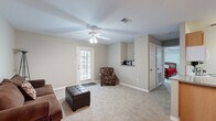 This efficient and thoughtfully designed single-floor residence offers a comfortable layout across one bedroom, one bathroom, and a combined living, dining, and kitchen area connected by a hallway. The living room features plush carpeting, a ceiling fan with integrated lighting, a private exterior door with a glass panel that brings in natural light, and a built-in shelf nook — creating a welcoming and functional space for relaxing or entertaining. The kitchen is well-equipped with warm wood-toned cabinetry, a peninsula with granite-style countertops, wood-look flooring, a white appliance suite including a refrigerator, electric range, microwave, and dishwasher, and ample upper and lower cabinet storage. Adjacent to the kitchen, the dining area is defined by rich hardwood-style flooring and an elegant chandelier overhead, offering an inviting setting for meals. The bedroom is a comfortable retreat with carpet flooring, a ceiling fan, a window for natural light, and a closet. The bathroom complements the space with wood-look flooring, a granite-style vanity with wood cabinetry, and a shower-tub combination. Neutral gray walls and consistent finishes throughout contribute to a cohesive, move-in-ready ambiance.