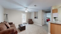 This efficient and thoughtfully designed single-floor residence offers a comfortable layout across one bedroom, one bathroom, and a combined living, dining, and kitchen area connected by a hallway. The living room features plush carpeting, a ceiling fan with integrated lighting, a private exterior door with a glass panel that brings in natural light, and a built-in shelf nook — creating a welcoming and functional space for relaxing or entertaining. The kitchen is well-equipped with warm wood-toned cabinetry, a peninsula with granite-style countertops, wood-look flooring, a white appliance suite including a refrigerator, electric range, microwave, and dishwasher, and ample upper and lower cabinet storage. Adjacent to the kitchen, the dining area is defined by rich hardwood-style flooring and an elegant chandelier overhead, offering an inviting setting for meals. The bedroom is a comfortable retreat with carpet flooring, a ceiling fan, a window for natural light, and a closet. The bathroom complements the space with wood-look flooring, a granite-style vanity with wood cabinetry, and a shower-tub combination. Neutral gray walls and consistent finishes throughout contribute to a cohesive, move-in-ready ambiance.