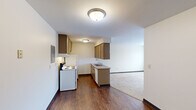 This single-floor unit offers a functional and efficient layout across three bedrooms, one bathroom, a kitchen, hallway, and closet. The kitchen features dark wood-tone cabinetry with ample upper and lower storage, a double-basin sink, a coil-burner electric range, refrigerator, and dishwasher. Rich hardwood-style flooring runs throughout the kitchen, which opens directly into the carpeted living area, creating a natural flow between spaces. Each of the three bedrooms is carpeted and finished with neutral walls, dark wood-trimmed windows, and baseboard heating units. Several bedrooms include windows that provide views of the surrounding area and allow natural light to fill the rooms. The primary bedroom features a built-in closet with sliding panel doors. One bedroom also includes a wall-mounted air conditioning unit for added climate control. The bathroom is well-appointed with a warm wood-toned vanity, a framed mirror, tile flooring, and a full tub-shower combination. Consistent dark baseboards throughout the unit provide a clean visual contrast to the light-colored walls. A dedicated closet adds practical storage to complement the overall layout of this compact, well-organized space.