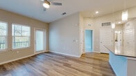 This well-appointed single-floor residence offers a thoughtfully designed open-concept layout that seamlessly connects the main living areas. The living room features warm wood-look luxury vinyl plank flooring, neutral beige-toned walls, recessed lighting, and a ceiling fan, creating a bright and airy atmosphere. Natural light filters in through blinded windows and a glass-panel door that opens to an outdoor area with greenery views.

The kitchen is a standout feature, showcasing crisp white shaker-style cabinetry extending to the ceiling, a white subway tile backsplash, dark quartz countertops, and a central island with pendant lighting overhead. Stainless steel appliances — including a range, over-the-range microwave, and refrigerator — complete the space, all set atop light hardwood-style flooring.

The bedrooms are finished with plush carpeting, ceiling fans, and generous windows that bring in ample natural light with views of surrounding trees. The primary bathroom is elegantly appointed with a dual-sink vanity featuring white cabinetry, a quartz countertop, framed mirrors, and wood-look flooring. A walk-in closet with wire shelving systems provides abundant organized storage. Throughout the residence, white panel doors and clean architectural lines contribute to a cohesive, modern aesthetic.