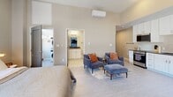 Located at 1501 Euclid Ave in Cleveland's vibrant Midtown corridor, this thoughtfully designed one-bedroom, one-bathroom unit maximizes every inch of its compact footprint. Soaring ceilings in the main living area create a sense of openness well beyond what the floor plan suggests, with neutral tones and soft carpeting lending a calm, modern ambiance throughout.

The spacious primary bedroom accommodates a full seating area alongside the sleeping space, enhanced by a wall-mounted ductless HVAC unit for individual climate control. An open kitchenette is outfitted with white shaker cabinetry, a textured tile backsplash, stainless steel refrigerator, dishwasher, and a deep sink — ideal for everyday living. A dining nook with a large wood-framed window brings in natural light and provides a comfortable spot for meals or work.

The bathroom features a clean, minimalist walk-in glass shower with matte black fixtures and crisp white surrounds. A vanity with ample counter space and warm lighting completes the bath. A dedicated in-unit laundry closet houses a stacked full-size washer and dryer with additional shelving, providing exceptional convenience rarely found at this scale. This unit offers a fully self-contained, efficient living experience in the heart of Cleveland.