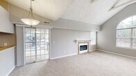 Located at 3800 Meriwether Dr in Durham, NC, this single-story, 2-bedroom, 2-bathroom home offers a well-planned layout with notable architectural character throughout. The living room immediately impresses with soaring vaulted ceilings, exposed beam detailing, and a striking arched window that floods the space with natural light. A stone-surround fireplace serves as the room's focal point, complemented by plush wall-to-wall carpeting and a neutral gray color palette. The expansive primary bedroom is a standout feature, boasting dramatic vaulted ceilings, sliding glass door access to an outdoor space, and generous proportions. It connects to a dedicated closet and its own bathroom, which includes a dark wood vanity with a light countertop and chrome fixtures and hardware. The second bedroom also features vaulted ceilings and a large window with outdoor views, providing ample natural light. Both bathrooms are well-appointed; one includes a full tub-shower combination with a chrome curtain rod. A dedicated laundry area with hardwood flooring accommodates a full-size washer and dryer alongside built-in overhead cabinetry and an additional closet for storage. Throughout the home, consistent gray tones and clean white trim create a cohesive and functional living environment.