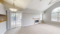 Located at 3800 Meriwether Dr in Durham, NC, this single-story, 2-bedroom, 2-bathroom home offers a well-planned layout with notable architectural character throughout. The living room immediately impresses with soaring vaulted ceilings, exposed beam detailing, and a striking arched window that floods the space with natural light. A stone-surround fireplace serves as the room's focal point, complemented by plush wall-to-wall carpeting and a neutral gray color palette. The expansive primary bedroom is a standout feature, boasting dramatic vaulted ceilings, sliding glass door access to an outdoor space, and generous proportions. It connects to a dedicated closet and its own bathroom, which includes a dark wood vanity with a light countertop and chrome fixtures and hardware. The second bedroom also features vaulted ceilings and a large window with outdoor views, providing ample natural light. Both bathrooms are well-appointed; one includes a full tub-shower combination with a chrome curtain rod. A dedicated laundry area with hardwood flooring accommodates a full-size washer and dryer alongside built-in overhead cabinetry and an additional closet for storage. Throughout the home, consistent gray tones and clean white trim create a cohesive and functional living environment.