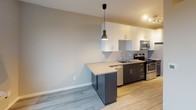 Located at 2333 Jackson St NE in the vibrant Northeast Minneapolis neighborhood, this single-floor unit showcases a thoughtfully designed, contemporary interior with a clean, modern aesthetic. Light gray wood-plank flooring runs throughout the space, creating a cohesive and polished look from room to room.

The kitchen is a standout feature, offering a functional galley-style layout with dark espresso lower cabinetry contrasted by crisp white upper cabinets. Stainless steel appliances — including a range, microwave, and dishwasher — complement the neutral countertops, while a peninsula with an integrated sink provides additional prep space and casual seating potential. A stylish pendant light anchors the kitchen area, adding a modern touch.

The living area is open and versatile, benefiting from generous natural light streaming through large windows that frame views of the surrounding residential neighborhood and mature tree canopy. The neutral warm-toned walls provide a welcoming backdrop throughout.

The bathroom maintains the same modern sensibility, featuring a dark-toned vanity with ample storage, a white integrated sink, and tile-style flooring that mirrors the rest of the unit. The layout is efficient and well-appointed with accessibility-friendly grab bar hardware.

Overall, this unit presents a well-executed modern design with quality finishes, an abundance of natural light, and a practical, open layout.