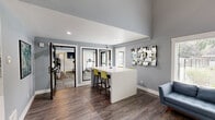 Located in Kent, Washington, this single-story community amenity facility offers a generously sized, well-appointed space designed to serve residents with comfort and functionality. The interior is characterized by a modern aesthetic, featuring cool gray walls, rich wood-look flooring, and soaring ceilings that create an open, airy atmosphere throughout.

The lobby entrance makes a strong first impression with its striking three-dimensional textured wall panel, accent lighting, and large glass entry doors that flood the space with natural light and provide views of the surrounding greenery. Adjacent to the entry, a welcoming lounge area is furnished with contemporary seating, including a tufted blue sofa and vibrant chartreuse accent stools, creating an inviting gathering space.

A central high-top bar counter with bar-height seating serves as a flexible workspace or social hub, while a dedicated fitness center—accessible via glass-paneled doors—houses exercise equipment and benefits from natural light and a bright, energizing layout.

Outside, a large outdoor swimming pool is the centerpiece of the exterior amenity space, framed by mature deciduous and evergreen trees that provide shade and a lush, park-like setting. The pool deck offers ample room for lounging, with poolside seating and a fenced perimeter ensuring privacy and safety. The combination of polished interiors and inviting outdoor spaces makes this facility a standout community resource.