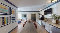 Located at 2200 House Creek Trail in Raleigh, NC, this single-floor community amenity space is thoughtfully designed to serve as a versatile gathering hub. The layout is divided into several interconnected zones that flow seamlessly into one another, creating a cohesive yet functionally distinct environment.

The lounge area is a standout feature, characterized by tray ceilings painted in a bold navy blue that adds depth and visual interest. Comfortable seating arrangements include upholstered armchairs with nailhead trim, modular blue ottoman cubes, and neutral sofas accented with teal and orange throw pillows. Patterned area rugs and warm hardwood-style flooring tie the space together, while an array of framed artwork adorns the walls. Large windows dressed with floor-length curtains flood the room with natural light and offer views of the outdoor pool area.

A generous dining zone accommodates a long communal table flanked by leather chairs, ideal for group gatherings or meetings. Colorful gallery-style artwork lines the walls, reinforcing the space's creative aesthetic.

The kitchenette is well-appointed with granite countertops, a tile backsplash, white cabinetry, a stainless steel under-counter refrigerator, a sink, and open shelving. A wall-mounted television above the counter adds convenience. Restroom facilities are also accessible from this area, making the space fully self-contained for events and everyday use.