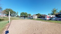 Located at 7150 Bent Tree Boulevard in Columbus, Ohio, this single-level outdoor recreational space offers a well-maintained community amenity area designed for active outdoor enjoyment. The centerpiece of the space is a full sand volleyball court, complete with a regulation net, set against a backdrop of mature trees and open green lawn. The natural sand surface provides an ideal playing area, while the surrounding landscape contributes a welcoming, park-like atmosphere under open skies. Adjacent to the volleyball court, a gazebo or covered structure is visible, suggesting additional gathering space for residents. A swimming pool area can also be seen nearby, further reinforcing the recreational character of the grounds. The community setting is framed by residential buildings and lush, mature trees that provide shade and a sense of enclosure, enhancing the overall outdoor ambiance. The grounds are well-kept, with neatly maintained grass and clear sightlines across the amenity area. This space serves as a central hub for outdoor activity and community engagement, offering a variety of recreational options within a single, cohesive outdoor environment.