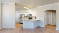 Located at 8110 S 107th E Ave in Tulsa, Oklahoma, this single-floor residence offers a well-designed, open layout with a blend of functional and comfortable living spaces. The kitchen is a standout feature, equipped with stainless steel appliances including a refrigerator, range, microwave, and dishwasher, all set against crisp white cabinetry and light stone countertops. A peninsula-style breakfast bar extends the counter space and connects the kitchen seamlessly to the main living areas, which are finished with light wood-style flooring throughout. Crown molding adds a refined architectural touch to the main living areas. The spacious living room is highlighted by a tile-surround fireplace, a ceiling fan, and an abundance of natural light streaming through multiple windows, including a charming bay window arrangement. An arched doorway provides a graceful transition between rooms. The bedrooms are carpeted for comfort, each featuring ceiling fans and windows with blinds. Additional rooms include a bathroom with a full tub/shower combination, white cabinetry, and wood-style flooring. The overall color palette is neutral and light, creating a bright, welcoming ambiance throughout the home.