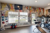 Located at 400 Southwest Pkwy in College Station, TX, this fitness center offers a thoughtfully designed, single-level workout space with a dynamic and energizing atmosphere. The standout architectural feature is a bold, colorfully painted exposed brick accent wall that runs along one side of the room, adding a striking artistic element to the space. Recessed lighting and dual ceiling fans throughout ensure the area remains well-lit and comfortable during workouts.

The fitness center is comprehensively equipped to support a full range of exercise routines. Cardio equipment includes treadmills, stair climbers, a stationary bike, and a rowing machine. Strength training is well-represented with a multi-station cable machine, a full dumbbell rack, medicine balls, resistance tools, and adjustable benches. A floor-to-ceiling mirror wall enhances the sense of space and aids in form monitoring.

Rubber flooring throughout provides durability and impact absorption. Large windows along the exterior walls invite generous natural light and offer views of the surrounding greenery and outdoor areas, creating an open, airy feel. A wall-mounted flat-screen TV adds an entertainment option for users. A glass door provides convenient direct access to the exterior. The overall ambiance is modern, motivating, and well-maintained, making this fitness center a functional and visually engaging amenity.
