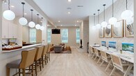 Located at 166 Caldy Knoll Dr in Sunbury, Ohio, this single-story community clubhouse spans a generously sized floor plan designed to serve as a comprehensive amenity hub. The space is defined by a bright, neutral color palette, light hardwood-style flooring, and soaring ceilings that create an open, welcoming atmosphere throughout.

The entrance corridor greets visitors with an elongated runner rug, structural columns, and transom windows above the main entry doors that flood the space with natural light. A staffed reception desk near the front features pendant lighting, white quartz countertops, and a wall-mounted display screen.

The main gathering area includes a comfortable lounge with seating and a billiards table, anchored by a striking stacked-stone fireplace. Adjacent is a business center with a row of desktop computers, cane-back chairs, and decorative textured wall panels beneath globe pendant lights.

The full kitchen is outfitted with white shaker cabinetry, quartz countertops, stainless steel appliances, and a lengthy island bar with counter seating. A windowed fitness center is also accessible, housing cardio and strength equipment with views of the surrounding greenery. A dedicated meeting/dining area rounds out the layout.