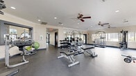 Located at 2252 N 44th St in Phoenix, AZ, this fitness center is a single-story facility thoughtfully designed to support a full range of workout routines. The space is divided into two dedicated exercise rooms connected by a hallway, offering users distinct zones for different types of training.

The main exercise room is generously proportioned, featuring durable rubberized flooring, recessed lighting, and ceiling fans that maintain air circulation throughout. Large arched windows invite abundant natural light and provide views of the surrounding outdoor environment, creating an open and energizing atmosphere. This room is equipped with a full rack of dumbbells, a Smith machine, weight benches, and a variety of cable and resistance machines, making it well-suited for comprehensive strength training.

A second exercise room provides dedicated space for cardio equipment, including treadmills and elliptical machines from True Fitness, all positioned in front of expansive arched windows. Wall-mounted televisions and additional ceiling fans enhance the comfort of this space. A connecting area features a spin bike and additional True treadmills, accented by a vibrant teal accent wall that adds a bold, motivating touch. Crown molding and full-wall mirrors throughout lend a polished finish to the facility, amplifying the sense of space and supporting proper form during workouts.