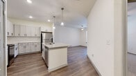 This single-floor unit offers a thoughtfully designed open-concept layout that seamlessly connects the kitchen and living areas. The kitchen serves as the centerpiece of the space, showcasing white shaker-style cabinetry with matte black hardware, granite countertops, and a full suite of stainless steel appliances, including a refrigerator, range, microwave, and dishwasher. A central island with an undermount sink provides additional workspace and casual dining potential, while pendant lighting adds a refined finishing touch. Wood-look plank flooring flows throughout the main living areas, adding warmth and visual continuity.

The living area extends naturally from the kitchen, offering generous space beneath a vaulted ceiling section, with recessed lighting enhancing the bright, airy atmosphere. A secondary room features neutral carpeting, a ceiling fan, and a window that invites natural light, making it well-suited as a bedroom or flexible-use space. An additional room with wood-look flooring, a ceiling fan, and a glazed door provides direct access to the exterior.

The bathroom is well-appointed with a dual-sink vanity, granite countertops, a tall storage cabinet, and a glass-enclosed walk-in shower with tile surround, delivering a clean, contemporary aesthetic throughout.