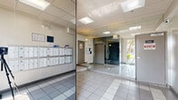 Located at 165 N Hoover St in Los Angeles, CA, this building entrance lobby serves as the primary access point for residents and visitors. The space is finished with light-colored square tile flooring that runs throughout, contributing to a clean and functional aesthetic. Floor-to-ceiling mirrored glass panels line portions of the interior walls, visually expanding the space and enhancing the brightness provided by recessed panel lighting in the drop ceiling above.

The lobby features a set of individual resident mailboxes mounted along the wall, offering a convenient mail collection area upon entry. Multiple gray interior doors provide access to stairwells and additional building areas, with signage posted near each. An elevator is also accessible directly from the lobby, ensuring ease of movement through the building.

Large glass entry doors at the front of the lobby invite natural light into the space and offer views of the landscaped exterior, including mature trees and a paved walkway. A textured entry mat at the threshold provides a transition from the outdoors. Wall-mounted sconce lighting adds supplementary illumination throughout the area. Overall, the lobby presents a practical and well-organized entry experience with a neutral, modern character suited to a multi-unit residential building.