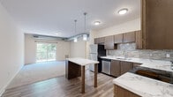 This thoughtfully designed 2-bedroom, 2-bathroom residence offers a functional single-floor layout encompassing a kitchen, living area, hallway, closet, and two full bathrooms. The kitchen serves as a central highlight, featuring rich dark-walnut cabinetry, a textured tile backsplash, light marble-style countertops, and a full suite of stainless steel appliances including a refrigerator, range, microwave, and dishwasher. A freestanding kitchen island with a marble-top surface and pendant lighting above adds both style and practicality. Wood-look plank flooring runs throughout the kitchen and living areas, transitioning seamlessly into plush carpeting in the living room, which opens to a private balcony via a sliding glass door, bringing in generous natural light and outdoor views. Both bedrooms are carpeted and well-lit by large windows that frame leafy outdoor scenery. The primary bedroom includes a dedicated closet with built-in shelving. Each bathroom is finished with wood-look tile flooring, dark-toned vanity cabinetry, and clean white countertops. One bathroom features a full tub-shower combination, while the second serves as a well-proportioned full bath. The overall aesthetic is clean, modern, and cohesive throughout.