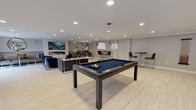 Located at 1177 Post Rd E in Westport, Connecticut, this contemporary amenity lounge is thoughtfully designed to offer a sophisticated social and recreational experience. The open-plan layout is anchored by light wood-look flooring, recessed lighting, and a neutral gray-and-white palette that lends the space a clean, modern aesthetic throughout.

At the heart of the space, two sleek pool tables with navy felt surfaces take center stage, illuminated by elegant pendant lighting overhead. Natural light streams in through multiple windows along the perimeter, enhancing the bright and airy atmosphere.

The lounge area provides a comfortable retreat with plush navy velvet armchairs, leather banquette seating, and coordinating accent pieces arranged around a striking linear gas fireplace. A bold abstract artwork in teal tones is mounted above the fireplace, adding a vibrant focal point to the seating zone. A multicolored area rug grounds the lounge and introduces a playful design element.

A generous L-shaped counter with a marble-style surface and bar-height seating serves as a versatile workspace or casual dining area, complete with a wall-mounted television above. Additional high-top bistro tables and bar stools provide supplementary seating options throughout the space. Together, these elements combine to create a well-appointed, multi-functional gathering area suited for both relaxation and entertainment.