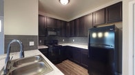 Located at 7600 Huntington Park Dr in Columbus, Ohio, this single-floor residence offers a thoughtfully designed living space with functional and attractive finishes throughout. The kitchen is a standout feature, showcasing rich, dark espresso-toned cabinetry that extends to the ceiling for ample storage. Light marble-look countertops provide a striking contrast against the dark cabinets, while a gray subway tile backsplash adds a contemporary, polished touch. The kitchen is equipped with black appliances, including a range with overhead microwave and a full-size refrigerator. A double-basin stainless steel sink rounds out the workspace. Wood-look flooring runs throughout the kitchen, adding warmth and durability underfoot. The overall design aesthetic balances bold, dark tones with lighter accents to create a space that feels both sophisticated and inviting. The single-floor layout ensures easy accessibility and a seamless flow between living areas. This residence at Huntington Park Drive offers a well-coordinated interior that is practical for everyday living while maintaining a refined visual appeal.