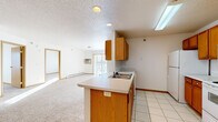 Located at 3301 14th St S in Moorhead, Minnesota, this two-bedroom, one-bathroom unit offers a practical and well-organized single-floor layout. The kitchen is a standout feature, equipped with warm oak cabinetry, white appliances including a range, microwave, and refrigerator, and a peninsula with a built-in sink that connects seamlessly to the living area. Light tile flooring runs throughout the kitchen, providing a clean contrast to the neutral carpet found in the living and bedroom spaces. The living room is generously sized, bathed in natural light from a sliding glass door that opens to an outdoor area and is fitted with a wall-mounted air conditioning unit and baseboard heating. Both bedrooms are carpeted and comfortably scaled, with the primary bedroom offering a double-door closet for ample storage. A second bedroom features its own window and baseboard heating. The bathroom includes a wood-toned vanity with storage, a large mirror with overhead lighting, and tile flooring. Consistent warm wood trim accents and light-toned walls give the unit a cohesive, neutral aesthetic throughout, making it a functional and move-in ready home.