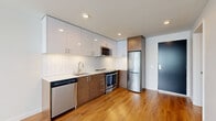 This 330 square foot studio apartment in Seattle offers a thoughtfully designed living space that maximizes functionality and style. The open-concept layout seamlessly blends the living area, kitchen, and sleeping space, creating a sense of spaciousness despite the compact footprint.

The kitchen is a standout feature, boasting sleek white upper cabinets contrasted with warm wood lower cabinets. Stainless steel appliances, including a refrigerator, dishwasher, oven, and over-the-range microwave, add a modern touch. The white tile backsplash and under-cabinet lighting enhance the kitchen's contemporary appeal.

Large windows flood the space with natural light, while horizontal blinds offer privacy control. The warm wood flooring throughout adds warmth and continuity to the space. The bathroom, though not pictured in detail, includes in-unit laundry facilities with a stacked washer and dryer.

Recessed lighting throughout provides ample illumination, and the neutral color palette creates a bright, airy atmosphere. The efficient design makes excellent use of the available square footage, offering a comfortable living environment in a prime Seattle location.