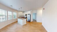 Located at 1 North Main Street in Port Chester, NY, this well-appointed two-bedroom, one-bathroom residence offers a thoughtfully designed single-floor layout with modern finishes throughout. The open-concept kitchen and living area serves as the heart of the home, anchored by a central island with a built-in sink and stone countertop, pendant lighting, and sleek white cabinetry complemented by a classic subway tile backsplash. Stainless steel appliances, including a refrigerator, range, and microwave, complete the contemporary kitchen. Natural light pours in through multiple windows, brightening the warm light hardwood flooring that runs seamlessly throughout the living spaces. A clean, white hallway connects the main living area to the private quarters, leading to two well-sized bedrooms with ample wall space and recessed lighting. The spacious primary bedroom includes access to a dedicated closet fitted with wire shelving for organized storage. The full bathroom features large-format tile flooring, a wood-toned vanity, and a walk-in glass-enclosed shower. The unit's crisp white walls, recessed lighting, and cohesive design create a bright, modern ambiance throughout this Port Chester residence.