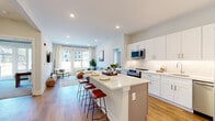 This well-appointed single-floor residence offers a thoughtfully designed open-concept layout that seamlessly connects the kitchen, dining, and living areas. The kitchen is a standout feature, showcasing crisp white shaker cabinetry extending to the ceiling, a subway tile backsplash, stainless steel appliances including a refrigerator, range, and built-in microwave, and a generously sized central island with quartz countertops and seating for multiple bar stools — ideal for casual dining or entertaining. Warm hardwood-style flooring runs throughout the main living areas, adding a cohesive and inviting feel.

The living room is bright and comfortable, benefiting from large windows and a glass door that invite abundant natural light and offer views of the surrounding urban environment. The space is well-proportioned and opens to the outdoor surroundings.

The bedrooms are carpeted and serene, each featuring large windows or glass doors that continue the theme of natural light. The primary bedroom includes ample space for a dresser and nightstands.

Two bathrooms serve the residence: one features a combined tub and shower with a large vanity mirror and grey cabinetry, while the second is finished with a similarly clean, neutral palette and dark wood cabinetry. Both bathrooms are tiled in light stone-toned flooring, maintaining a consistent modern aesthetic throughout the home.
