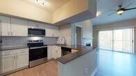 This well-appointed single-floor residence offers a thoughtfully designed open-concept layout with modern finishes throughout. The kitchen is a standout feature, equipped with stainless steel appliances including a range, microwave, dishwasher, and refrigerator. Crisp white shaker-style cabinetry, a classic subway tile backsplash, and dark quartz countertops create a clean, contemporary aesthetic. A peninsula with a breakfast bar provides additional counter space and connects the kitchen seamlessly to the adjacent living and dining areas. The living room is bright and airy, featuring vaulted ceilings, a ceiling fan, a fireplace with a white surround, and a sliding glass door that opens to a balcony with outdoor views. Light wood-tone flooring runs consistently throughout the space, enhancing the open and cohesive feel. Two well-sized bedrooms each offer ceiling fans and large windows that invite abundant natural light. Both bathrooms are finished in a modern style, featuring floating wood-toned vanities with white countertops and wood-look tile flooring. One bathroom includes a full shower-tub combination. The overall ambiance is clean, contemporary, and move-in ready.