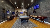 Located at 1717 Canvasback Lane in Columbus, Ohio, this single-floor community clubhouse is thoughtfully designed to provide an upscale entertainment experience. The grand lobby welcomes guests with soaring double-height ceilings, an eye-catching multi-bulb modern chandelier, large-format patterned tile flooring, and floor-to-ceiling windows that flood the space with natural light. Framed historical photography lines the upper walls, adding character and local context.

The centerpiece of the facility is a dramatic game room finished with stacked stone accent walls, a dark ceiling with recessed lighting, and warm hardwood flooring. A full-size pool table anchors the room beneath a geometric pendant light, while a shuffleboard table, classic arcade cabinet, and wall-mounted flat-screen televisions round out the entertainment offerings. Lounge seating with plaid upholstered chairs provides comfortable spots to relax between games.

An adjacent poker lounge continues the stacked stone aesthetic, featuring a dedicated round poker table with leather seating beneath a mid-century-style chandelier.

The kitchenette is equipped with dark cabinetry accented by brass hardware, white subway tile walls, open shelving, a beverage refrigerator, and a coffee station — all set atop vibrant encaustic-style mosaic tile flooring. A glazed entry door connects this area directly to the exterior, providing convenient access throughout the facility.
